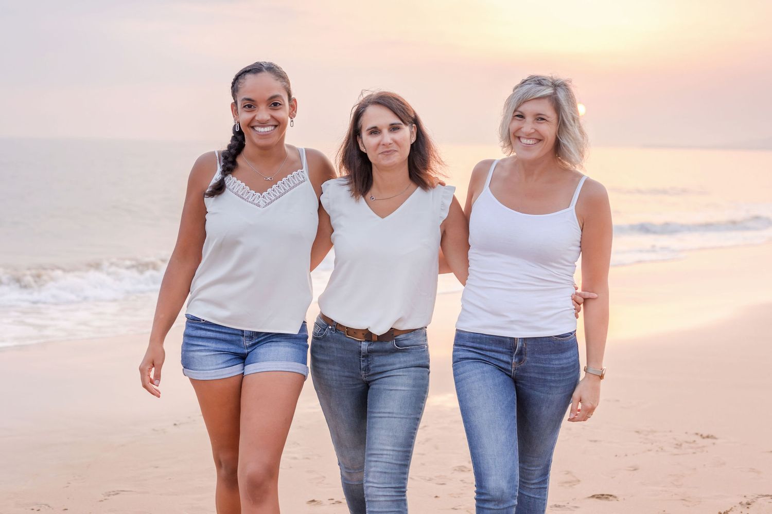 Three friends in casual summer attire walking along the beach at sunset.