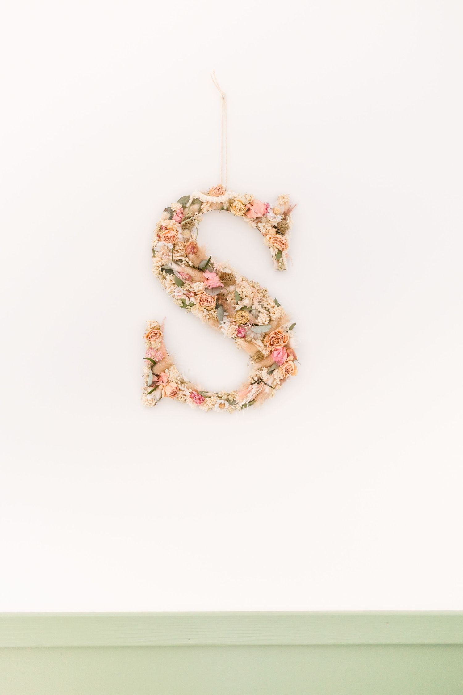 Decorative floral letter 'S' in pink and peach tones mounted on a mint green wall.