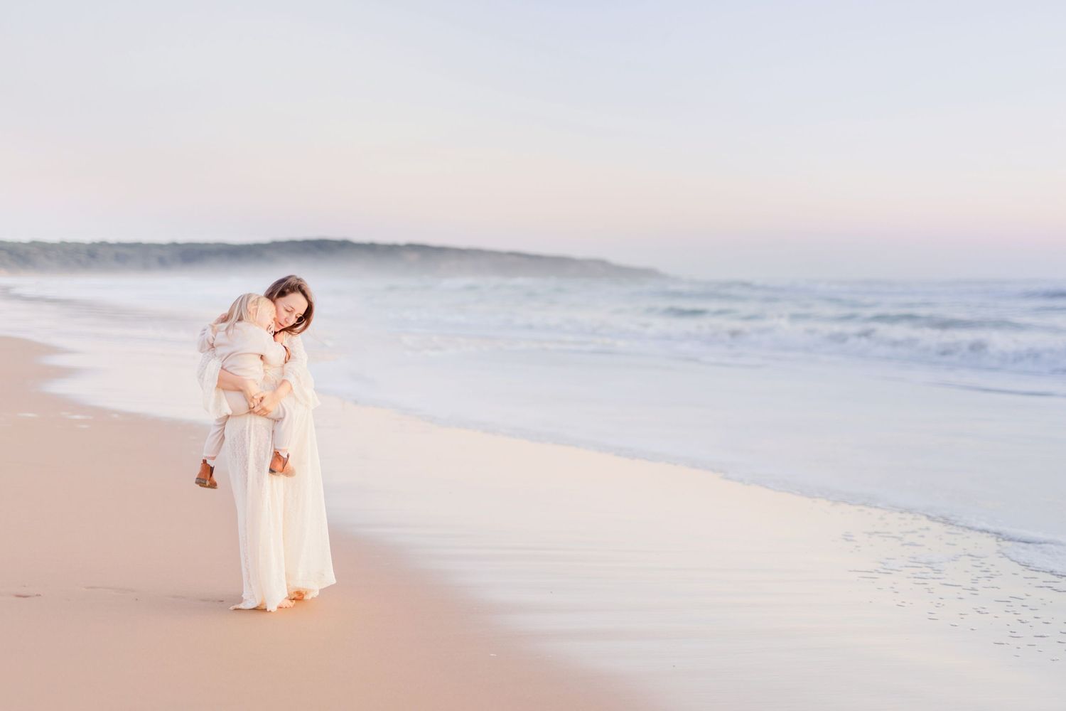 Family of two enjoying a tender moment while walking along a peaceful beach shoreline.