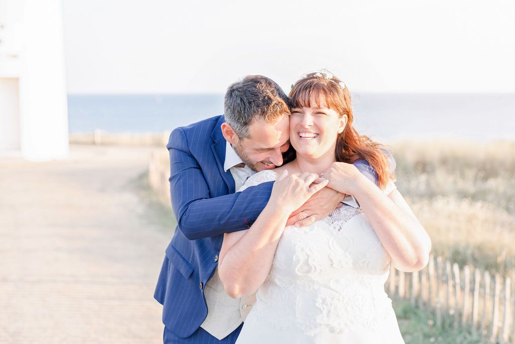 A loving wedding moment captured against a seaside lighthouse backdrop.