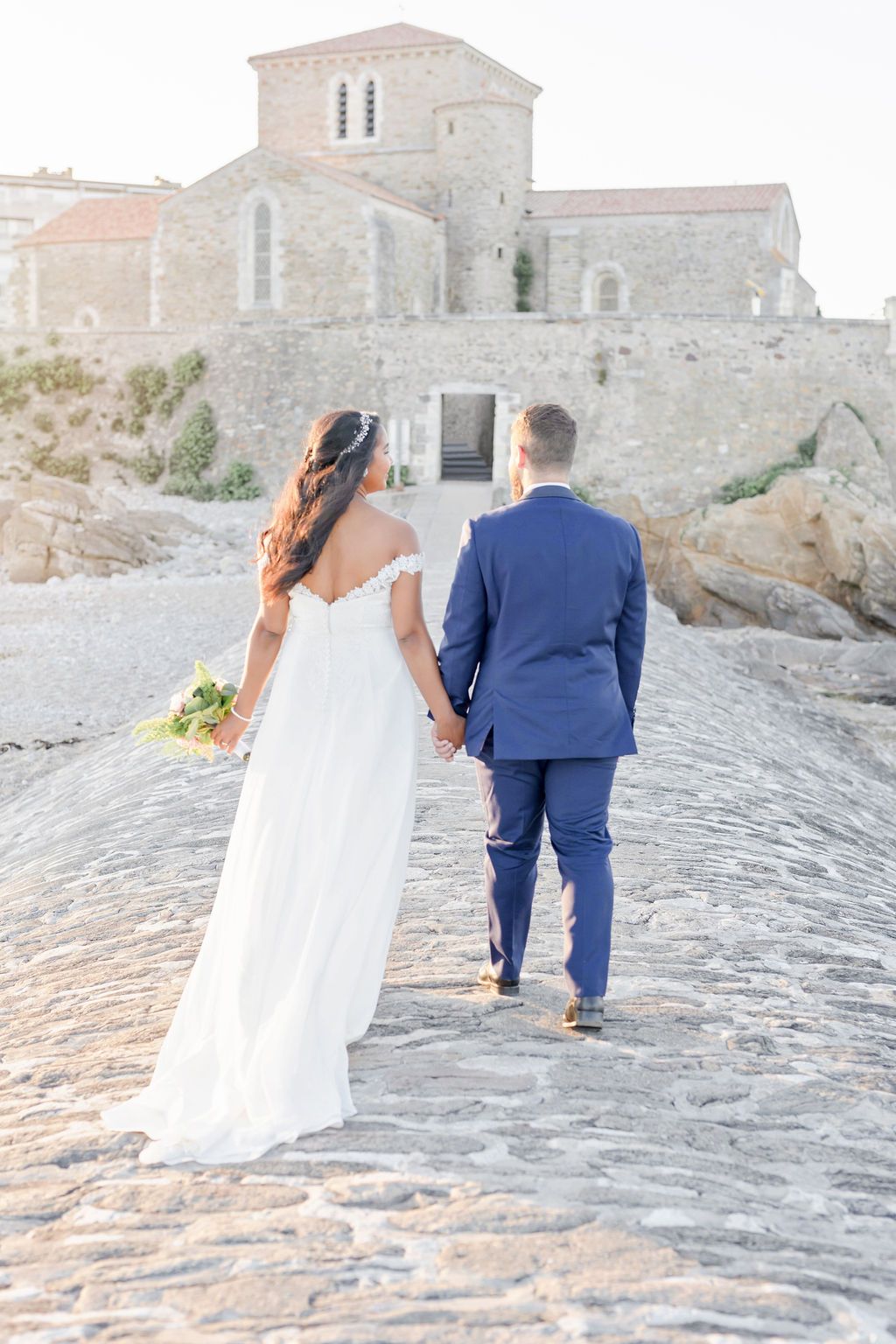 Newlyweds walking hand in hand up stone path towards historic church building.