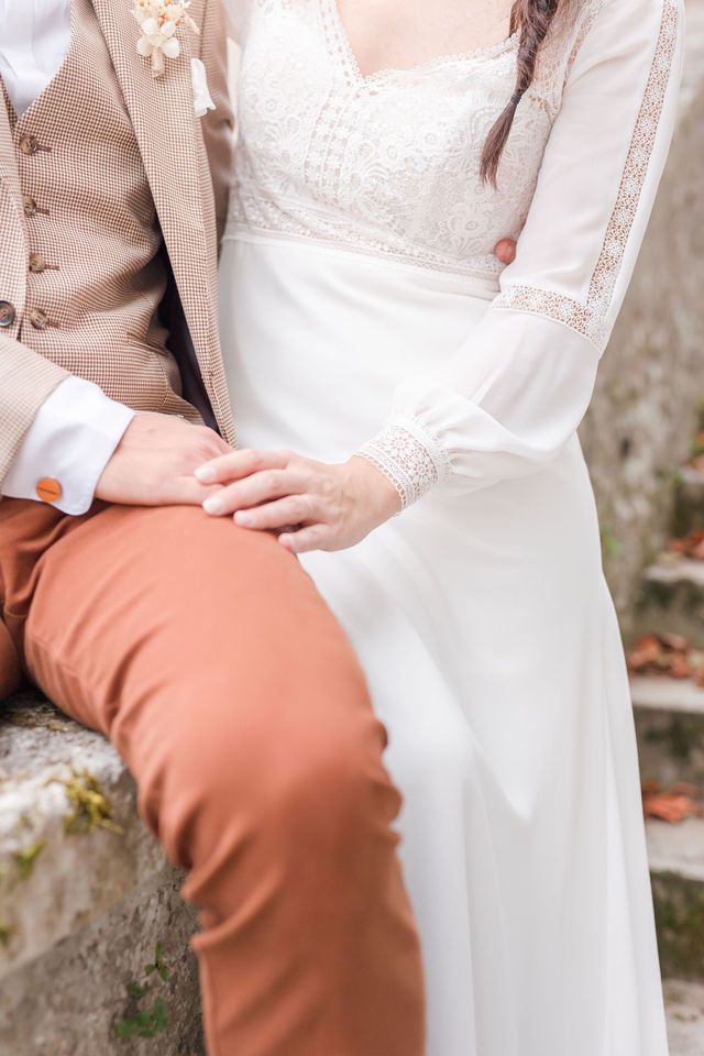 Close-up detail of vintage-style wedding attire showing lace dress and beige suit.