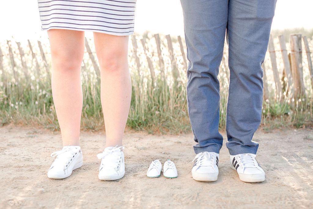 Two pairs of white sneakers with tiny baby shoes between them on a coastal path.