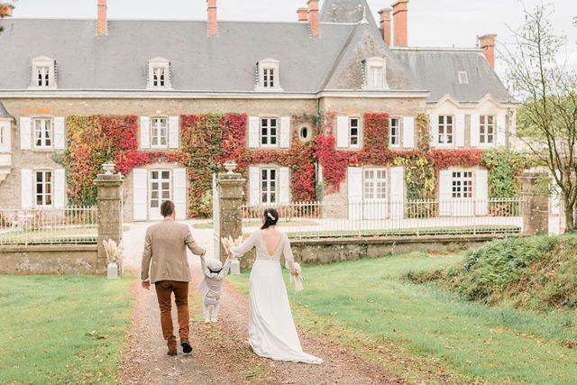 Elegant French chateau with stone walls and red shutters sits amid autumn foliage.