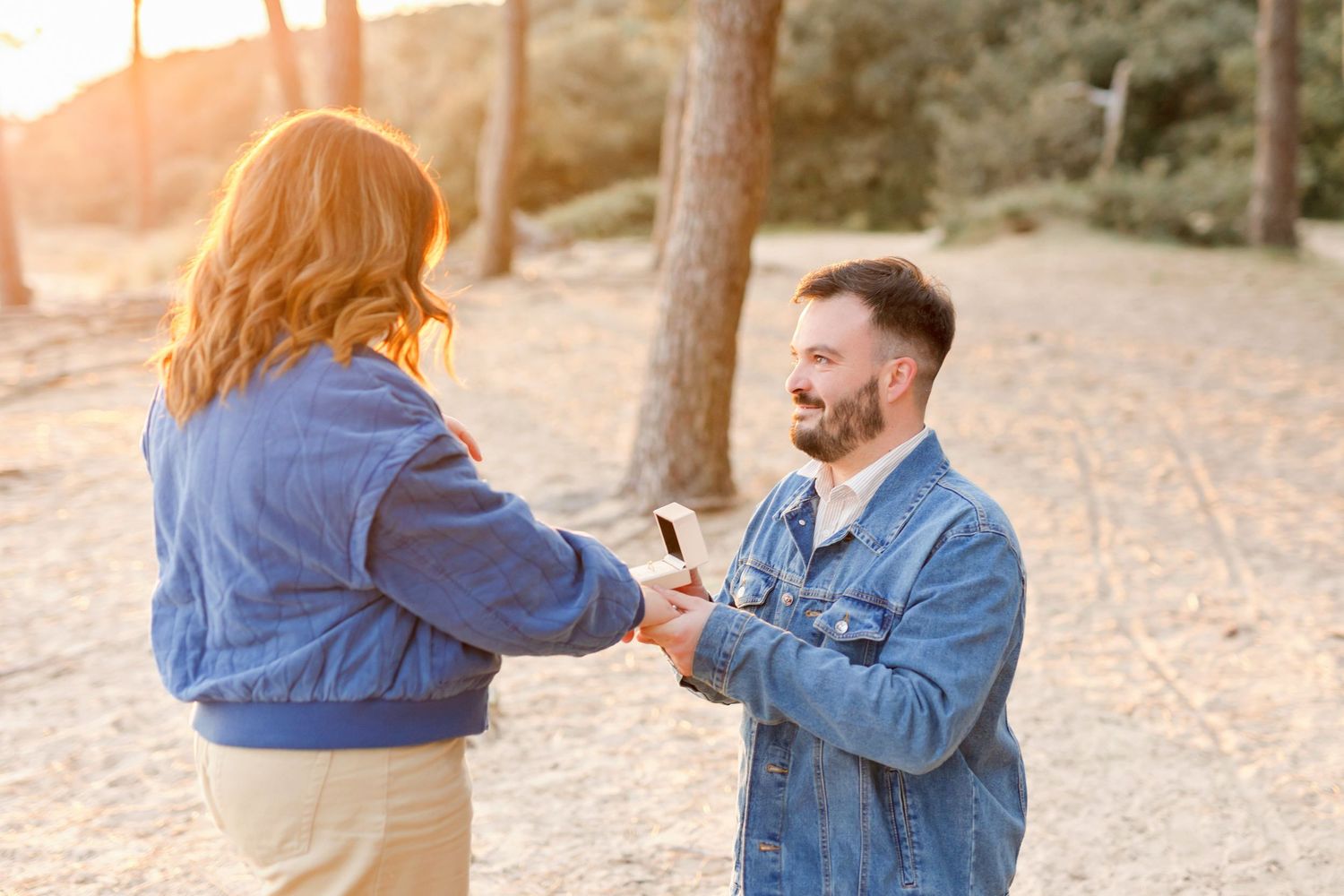 A couple in matching denim jackets sharing an intimate moment at sunset in a wooded area.