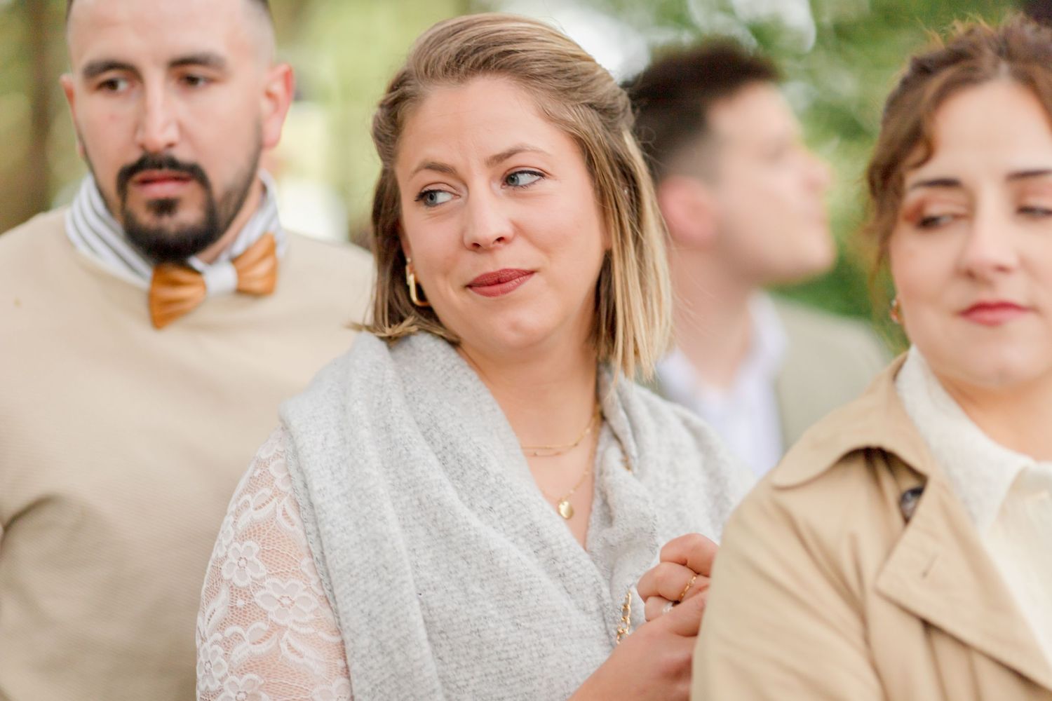 Wedding guests in casual attire smile during an outdoor forest ceremony.