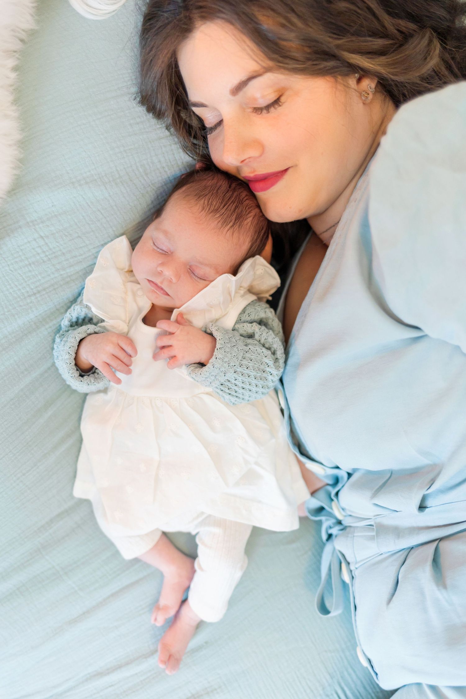 A peaceful moment captured with a sleeping baby in white and blue knit clothing on mint bedding.