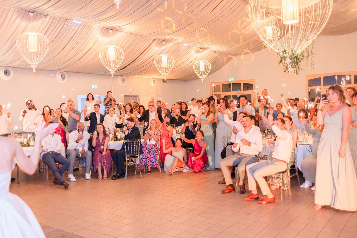 Wedding reception crowd cheers and celebrates with raised arms in decorated venue with draping.