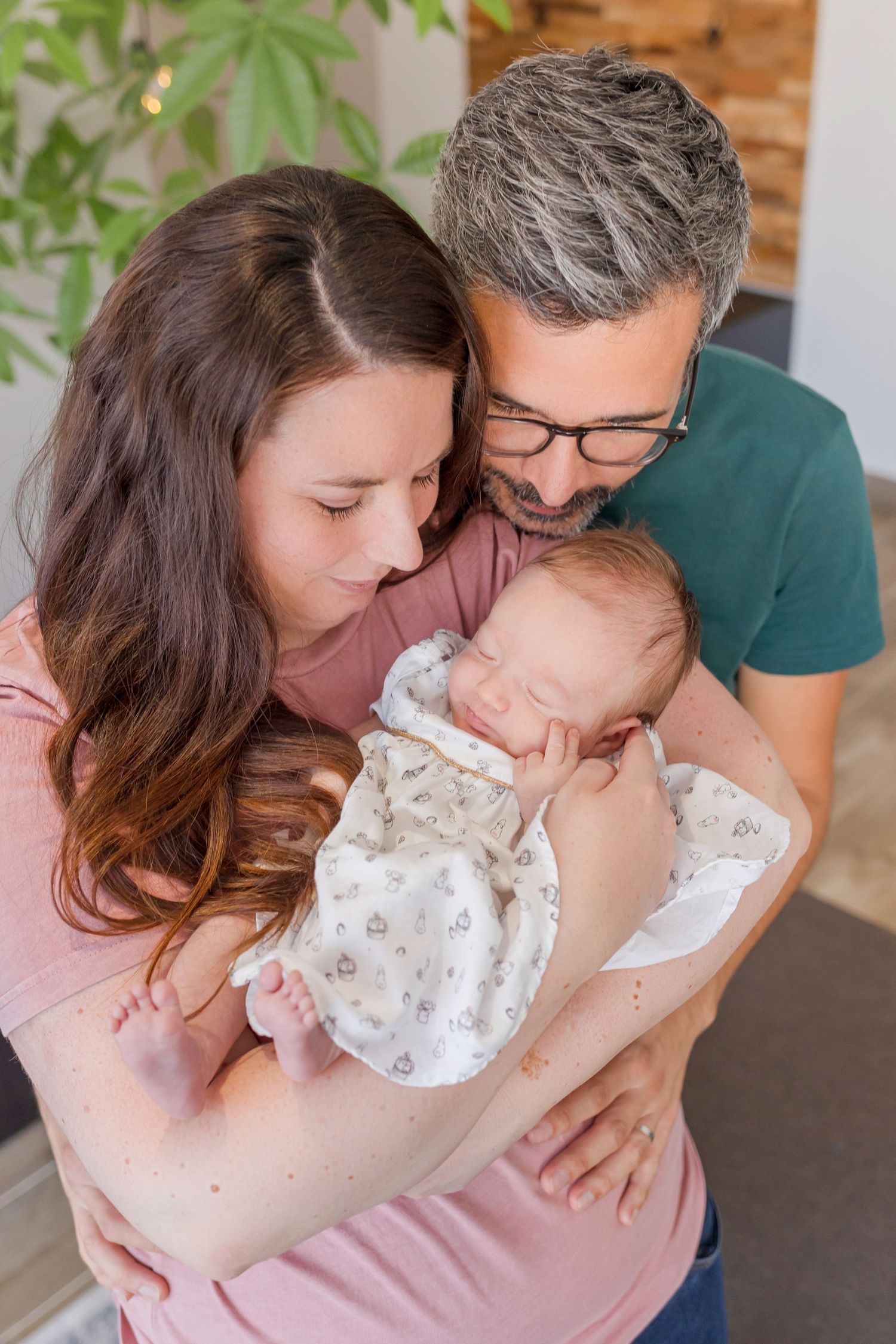 A baby in a white floral outfit is being lovingly embraced by family members.