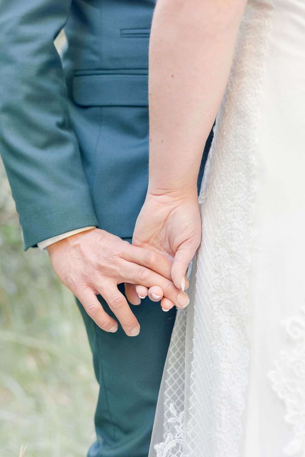 Close-up of couple holding hands showing wedding attire details.
