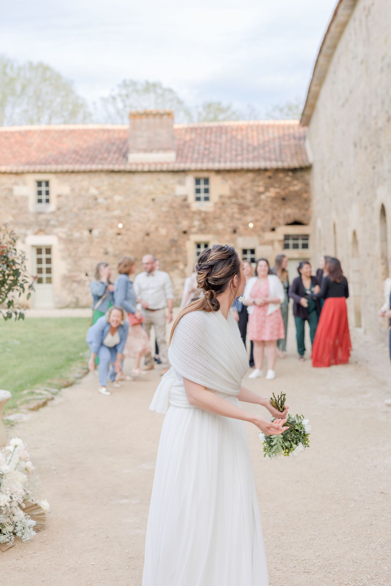 Elegant wedding celebration outside a rustic stone chateau with guests gathered in the courtyard.