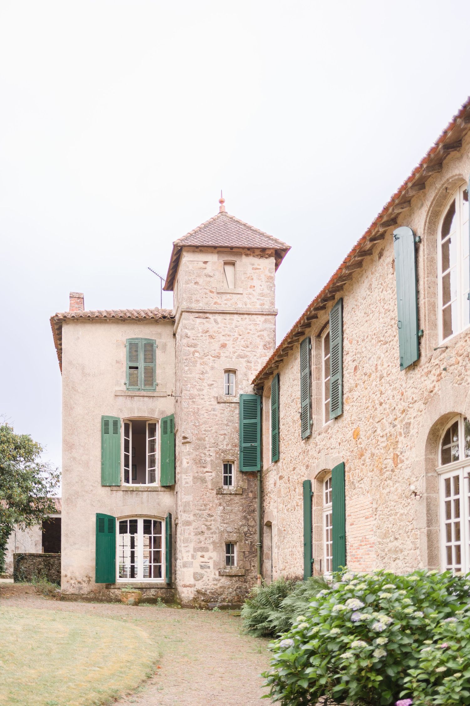 Historic French chateau with stone walls, green shutters, and a distinctive tower feature.