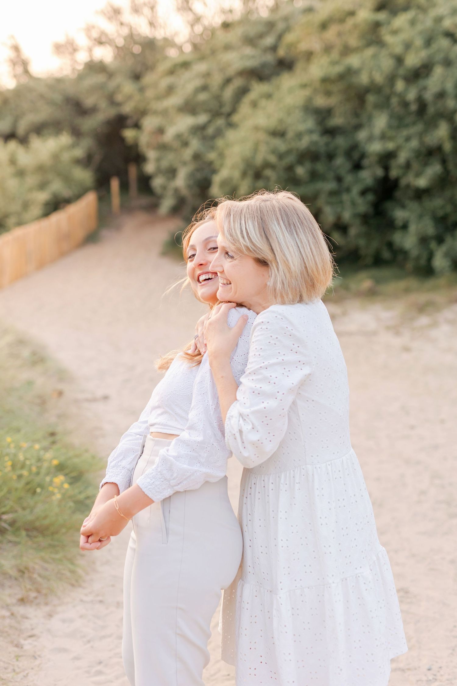 Two people in white outfits sharing a joyful moment on sandy path surrounded by greenery.