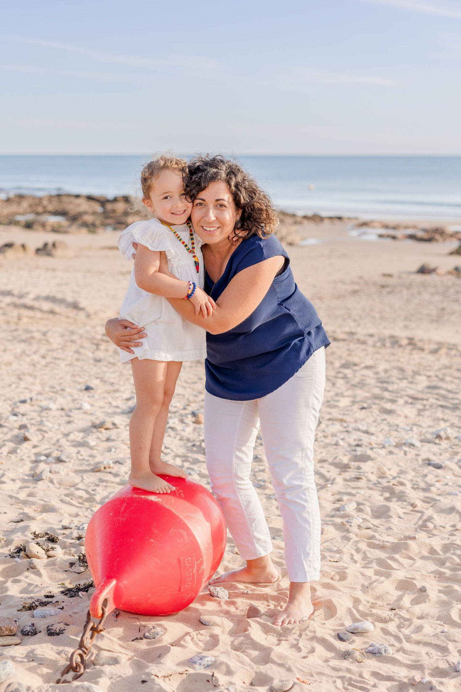 A playful beach moment with a large red buoy on sandy shores under blue skies.