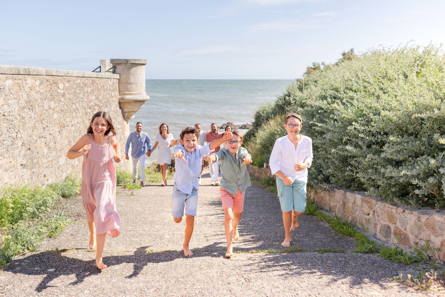 People walk along a scenic coastal path with historic stone walls and ocean views.