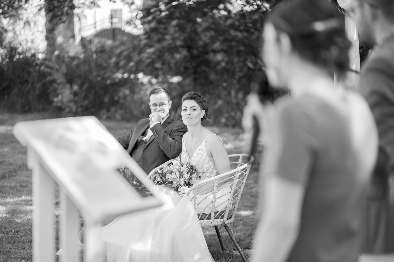 Black and white photo of couple seated during outdoor wedding ceremony.