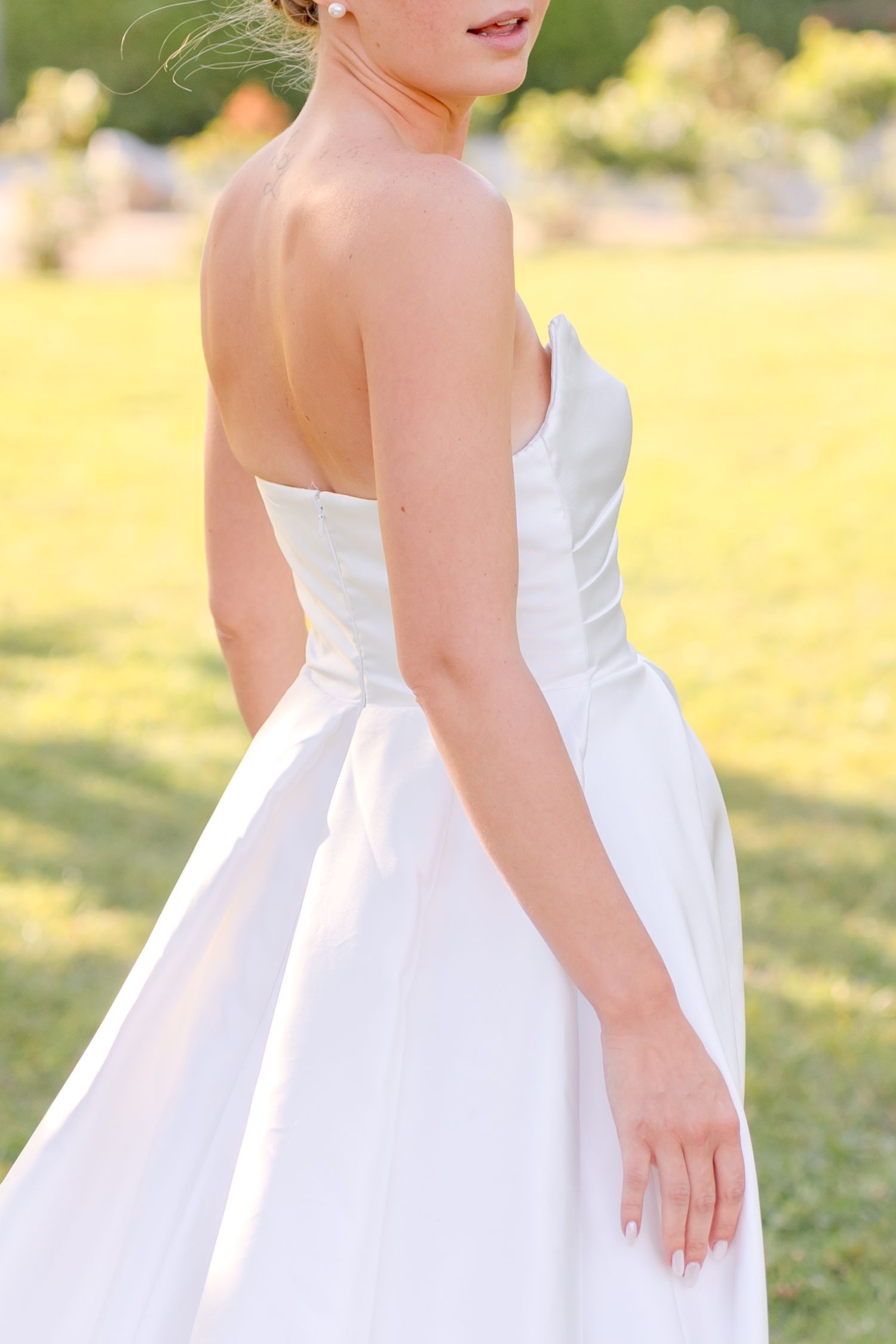 Close-up details of white wedding dress design in outdoor setting.