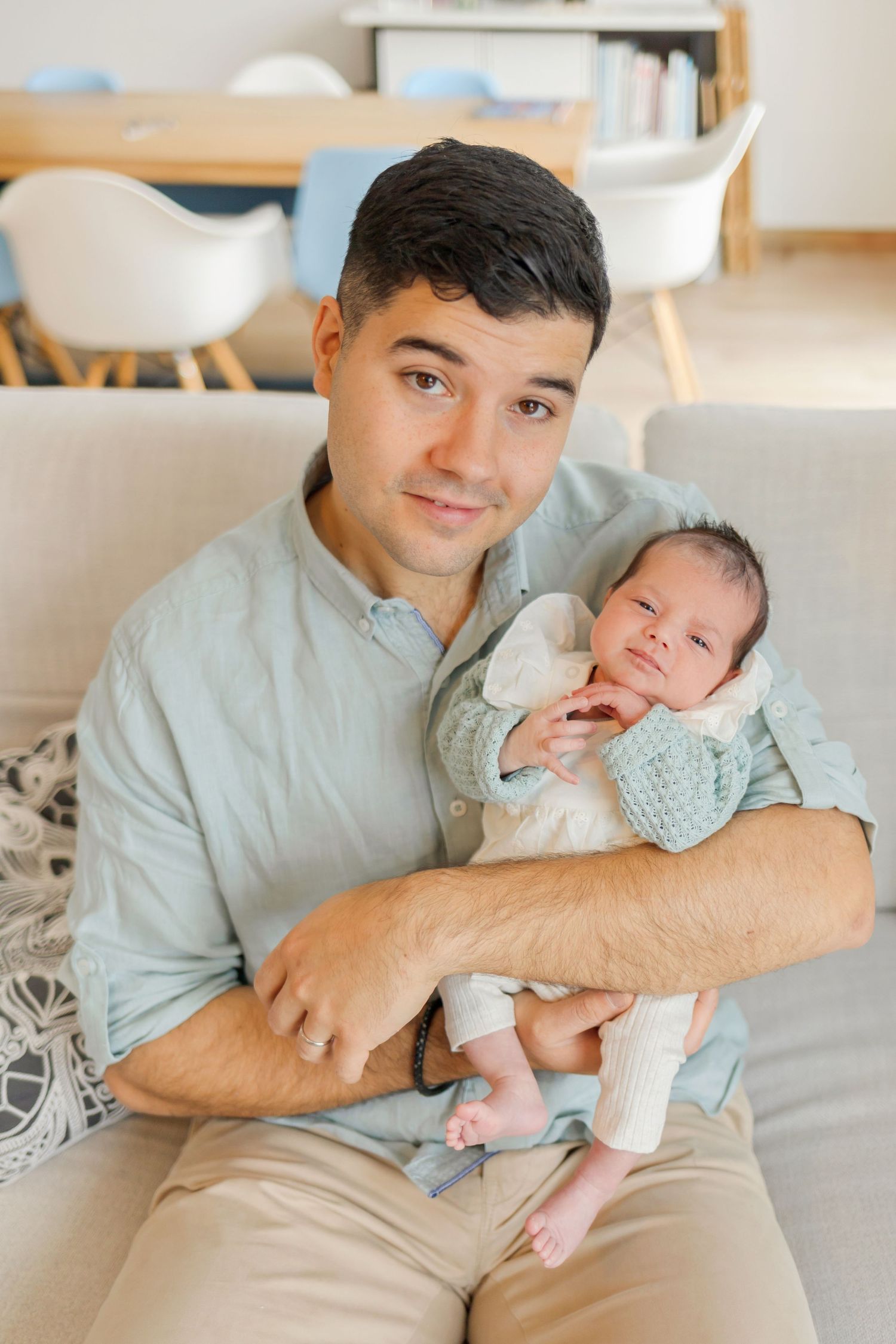 Parent in light blue shirt holding peaceful newborn on living room couch.