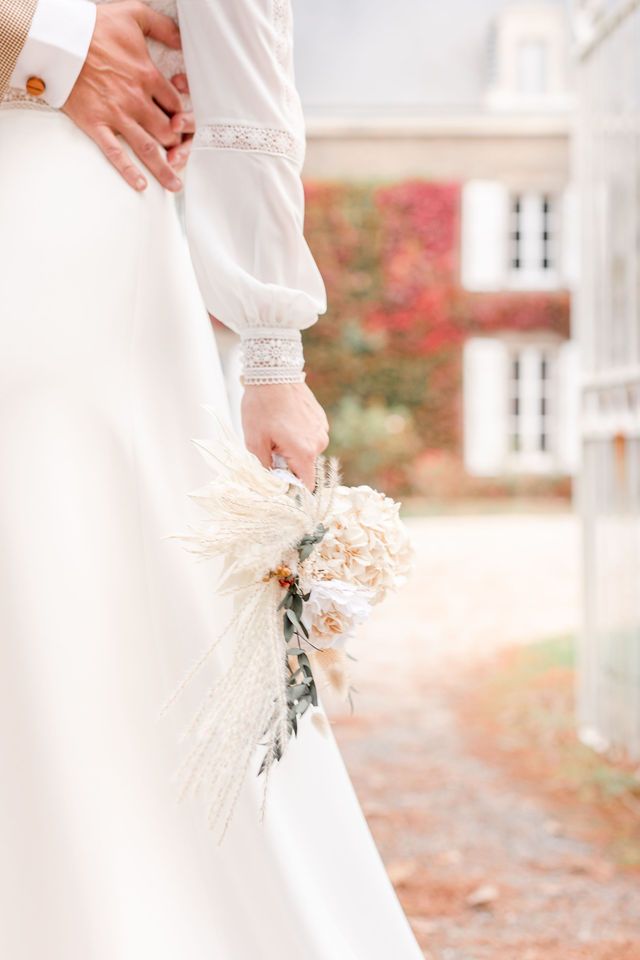 Close-up details of wedding dress lace and dried floral bouquet in soft natural light.