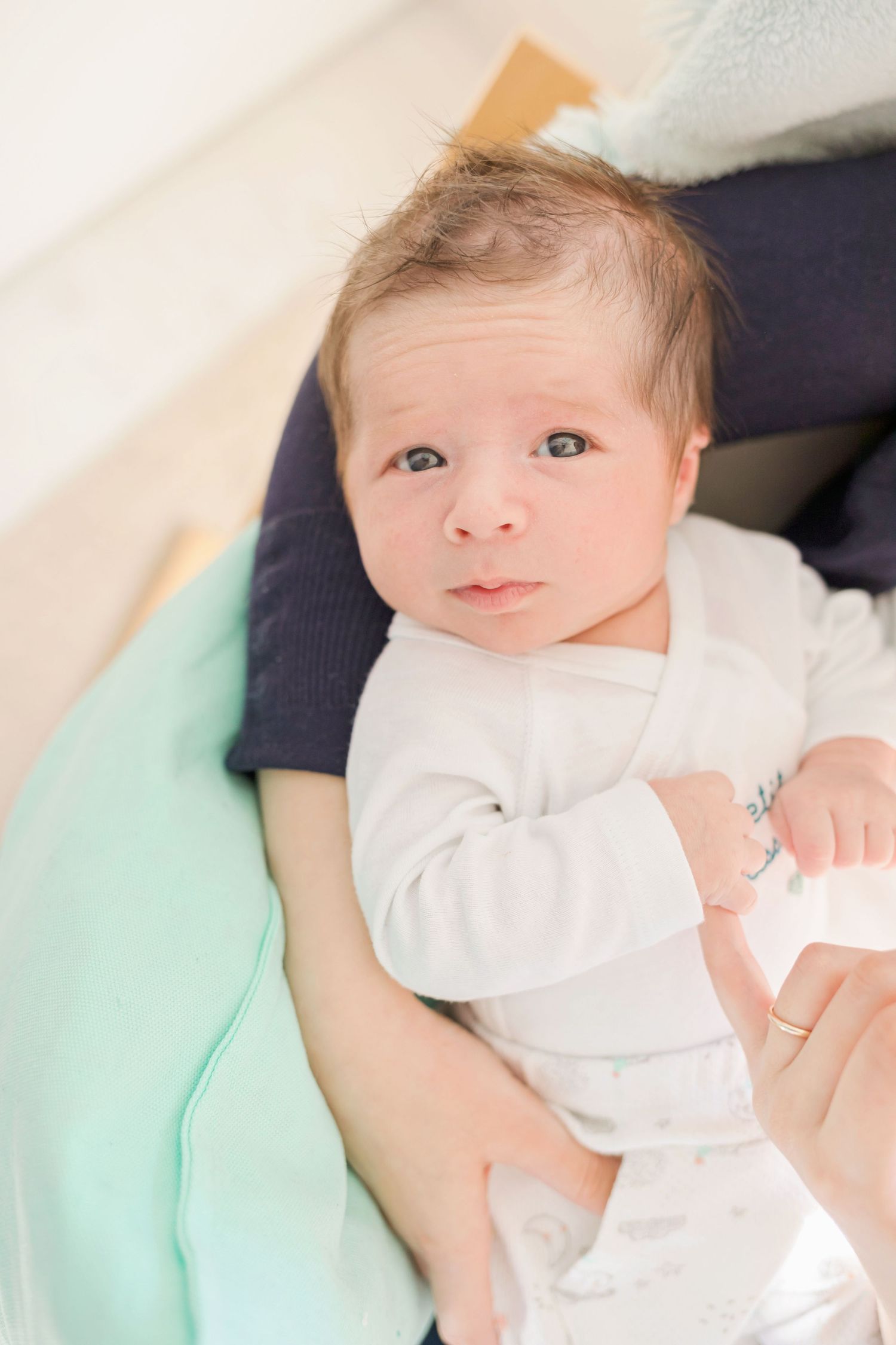Baby dressed in white lying on mint green changing pad.