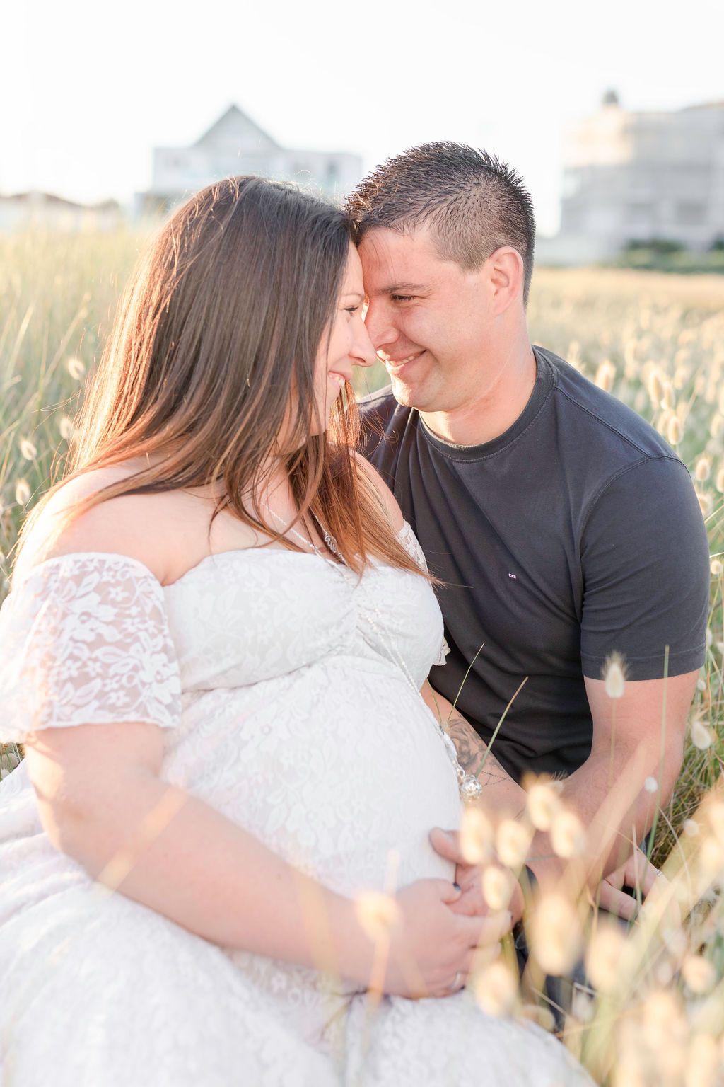 A romantic maternity photoshoot in a sunlit meadow features a couple sharing an intimate moment.