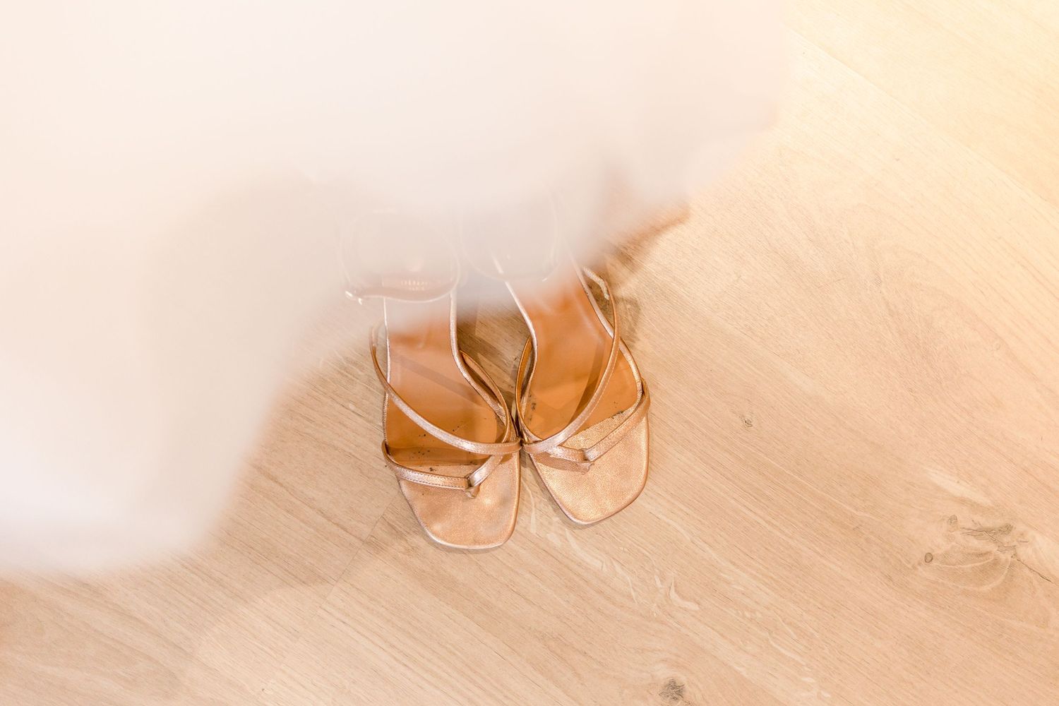 Gold bridal sandals on light wooden floor.