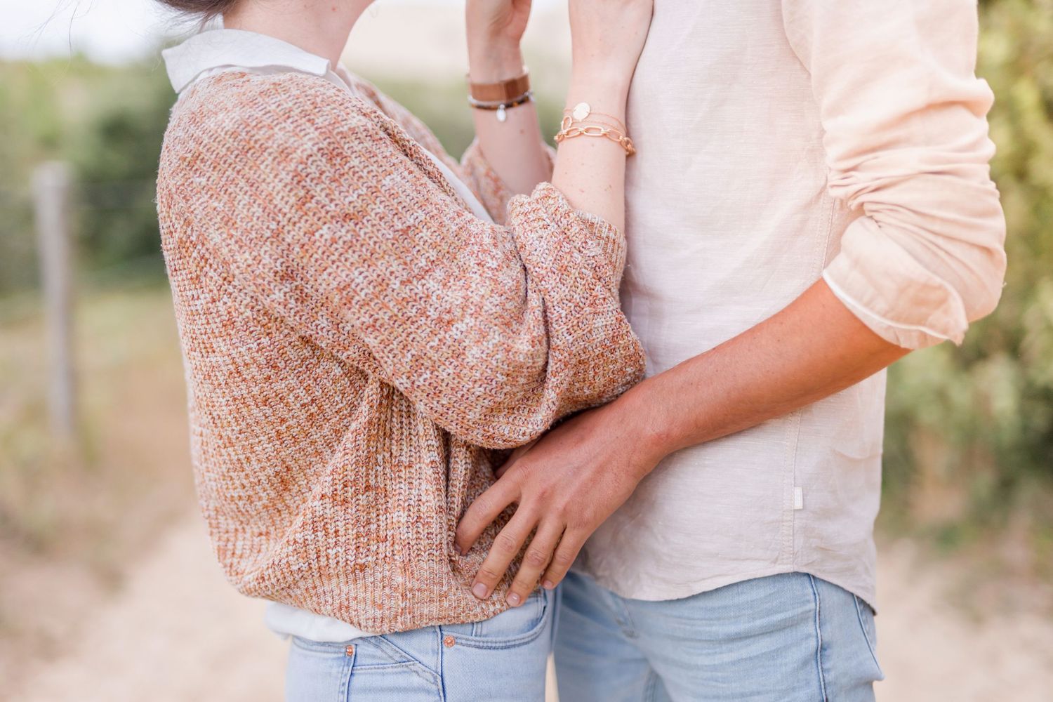 Couple embracing in casual sweater and shirt against nature background.