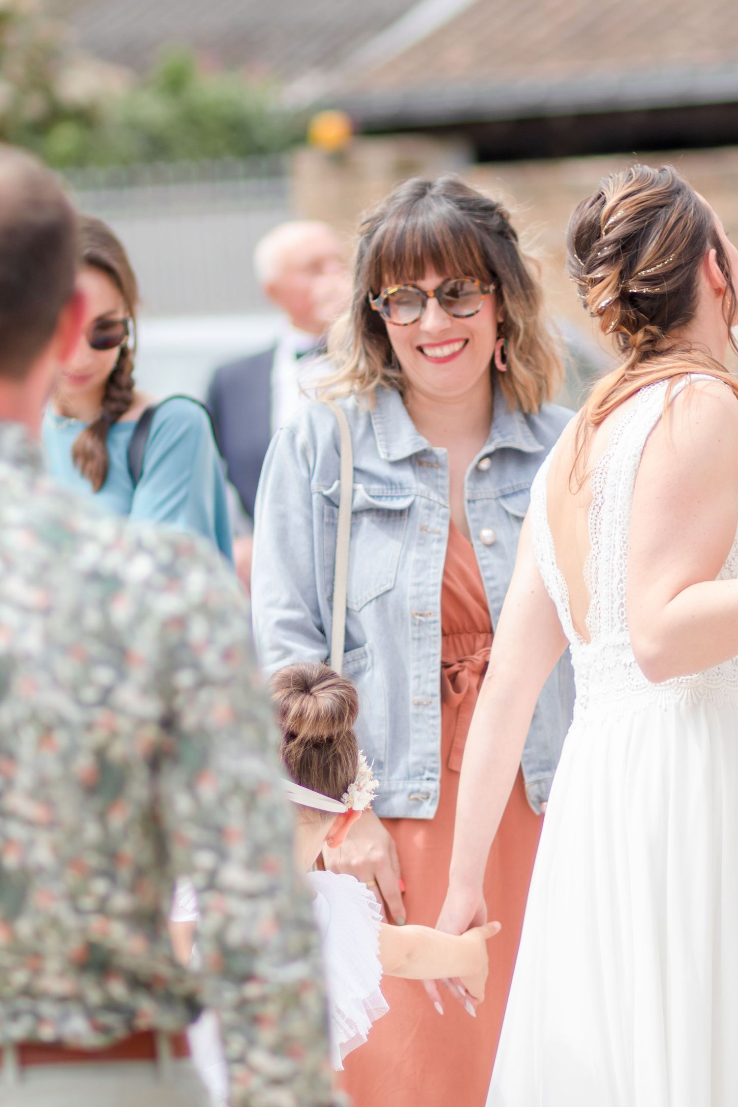 Wedding attendees in summer dresses and denim jackets gather for casual photos.