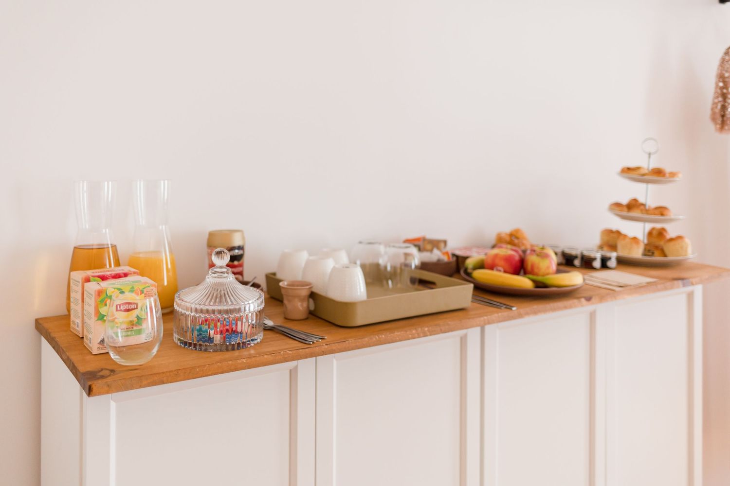 Breakfast buffet setup with pastries, jams, and drinks on white cabinet.