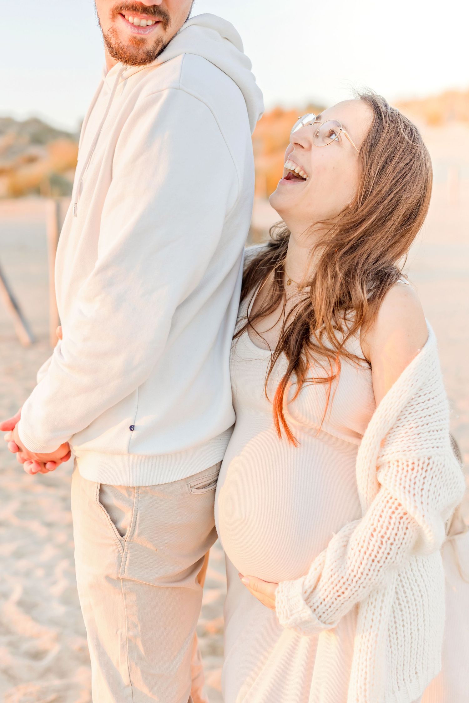 Two people embrace and laugh together on a sunlit beach.