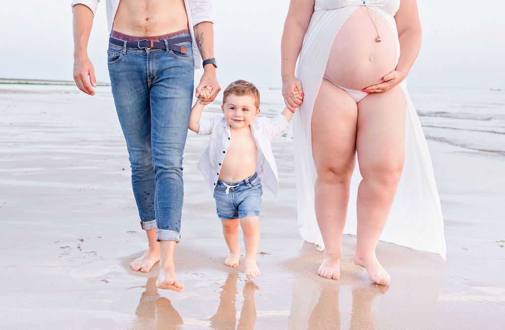 Family walking barefoot together on beach with waves in background.