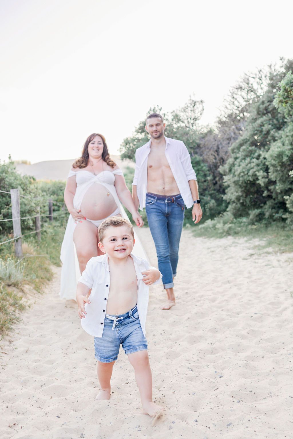 A carefree family maternity photo showing a child running ahead on a sandy nature trail.