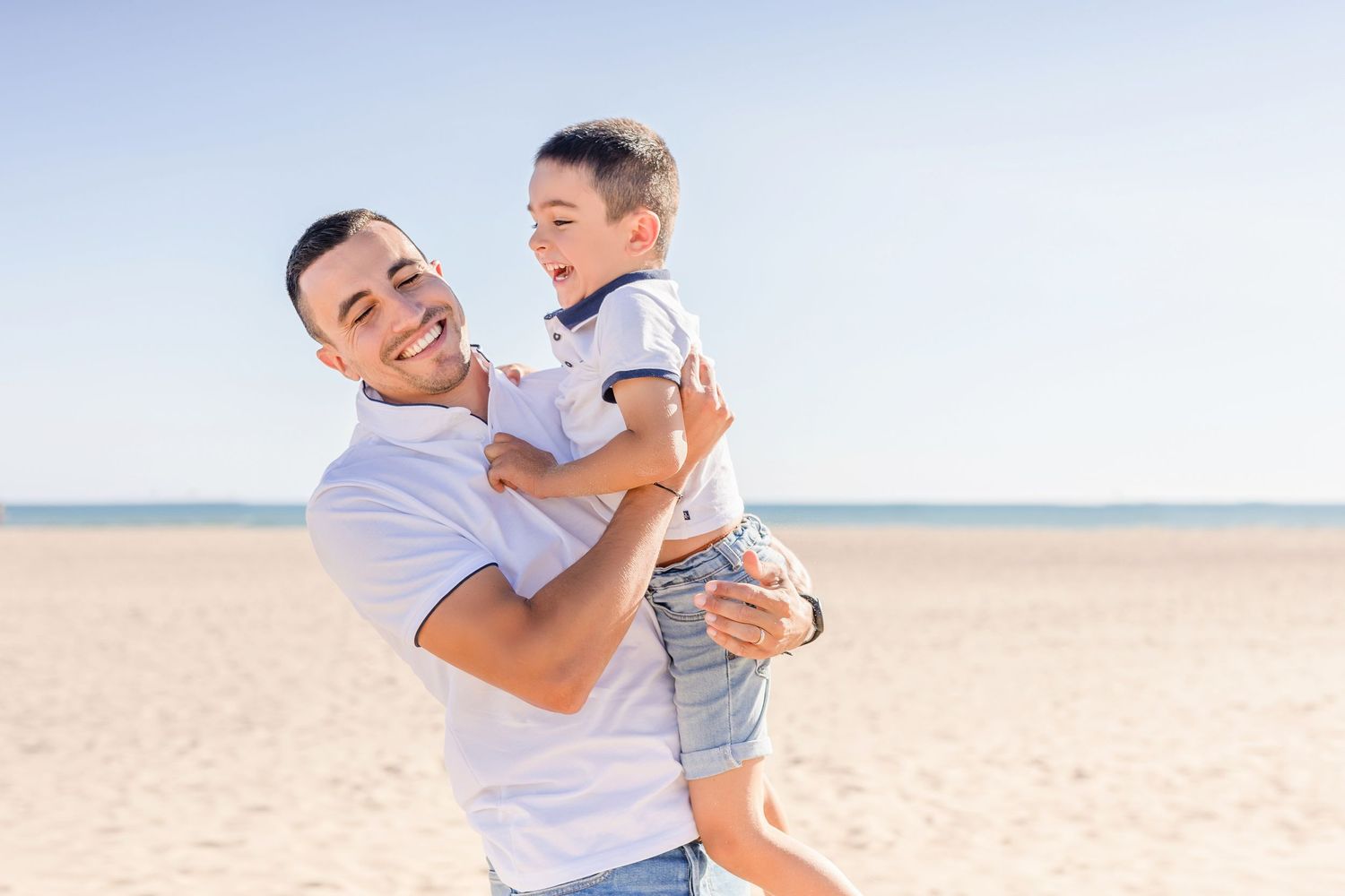 Joyful parent and child sharing a candid laughing moment on the beach.