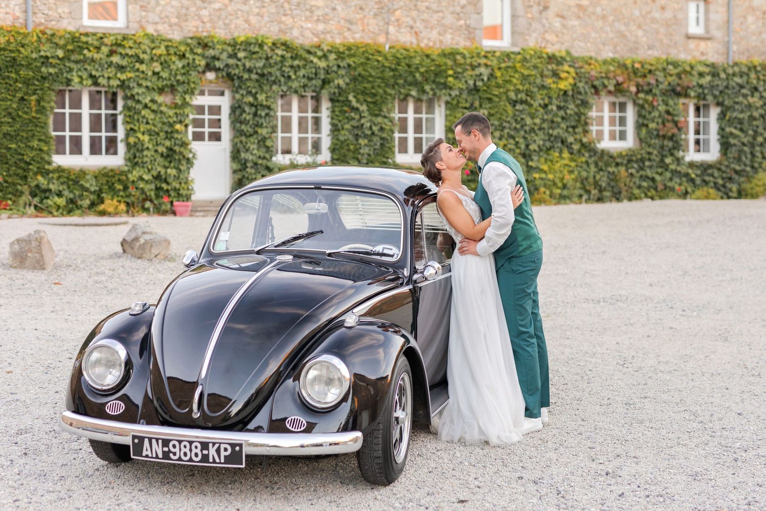 Classic black Volkswagen Beetle parked in front of an ivy-covered stone building during a wedding photoshoot.