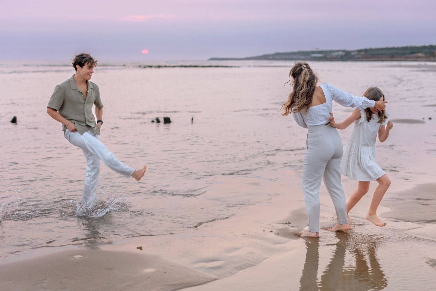 People playing and splashing in shallow beach water during sunset.