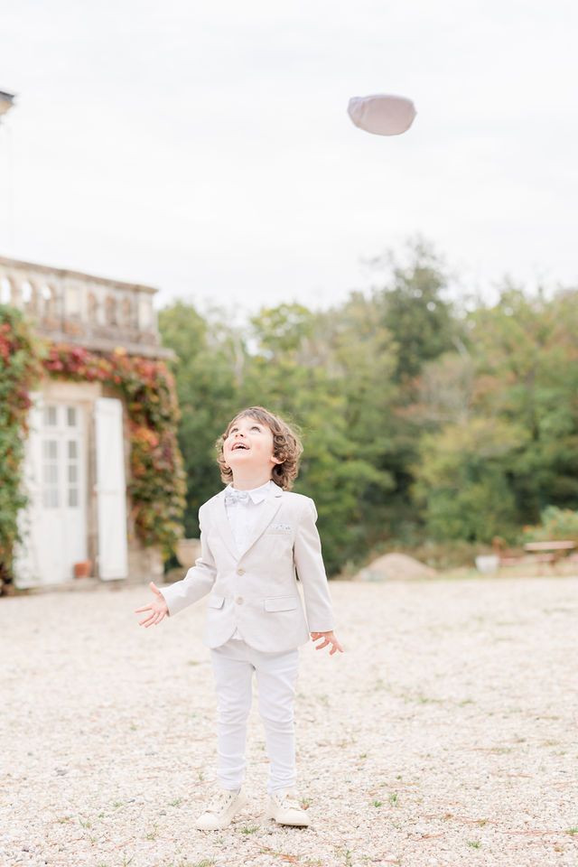 Child in all-white formal attire plays joyfully on gravel path near historic building.