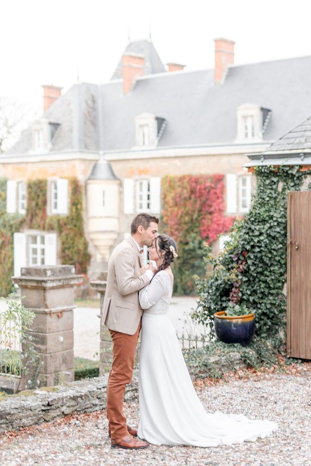 Romantic wedding portrait against historic French mansion with autumn foliage.