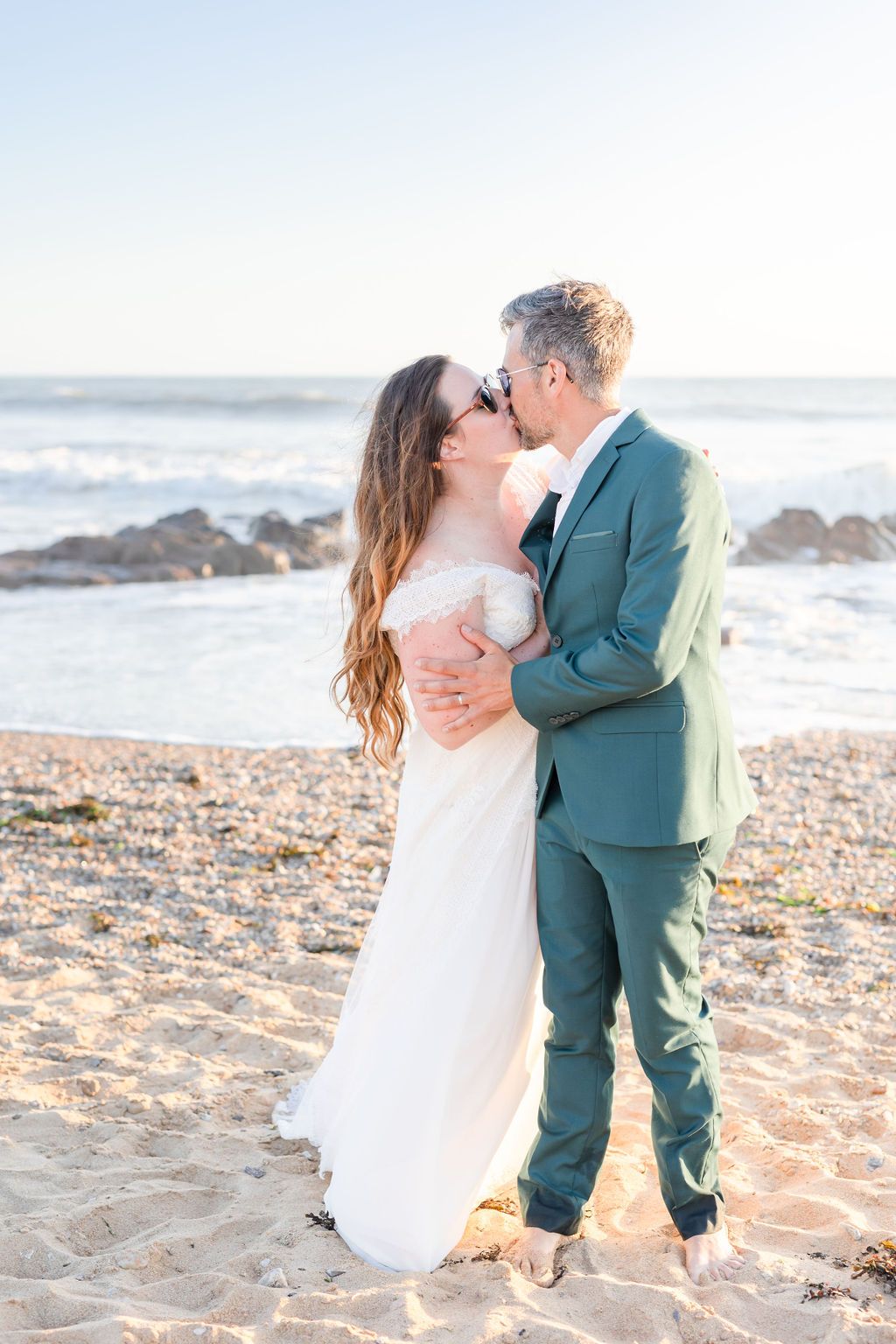 Romantic beach wedding portraits at sunset with couple embracing.