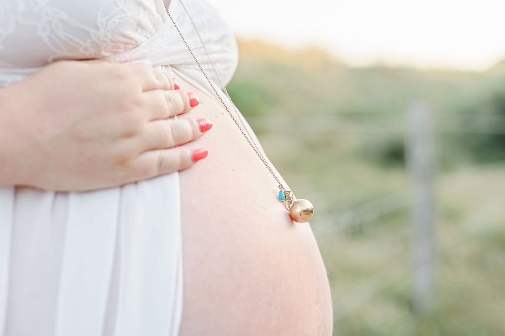 Close-up maternity photo showing hands cradling belly against white dress.