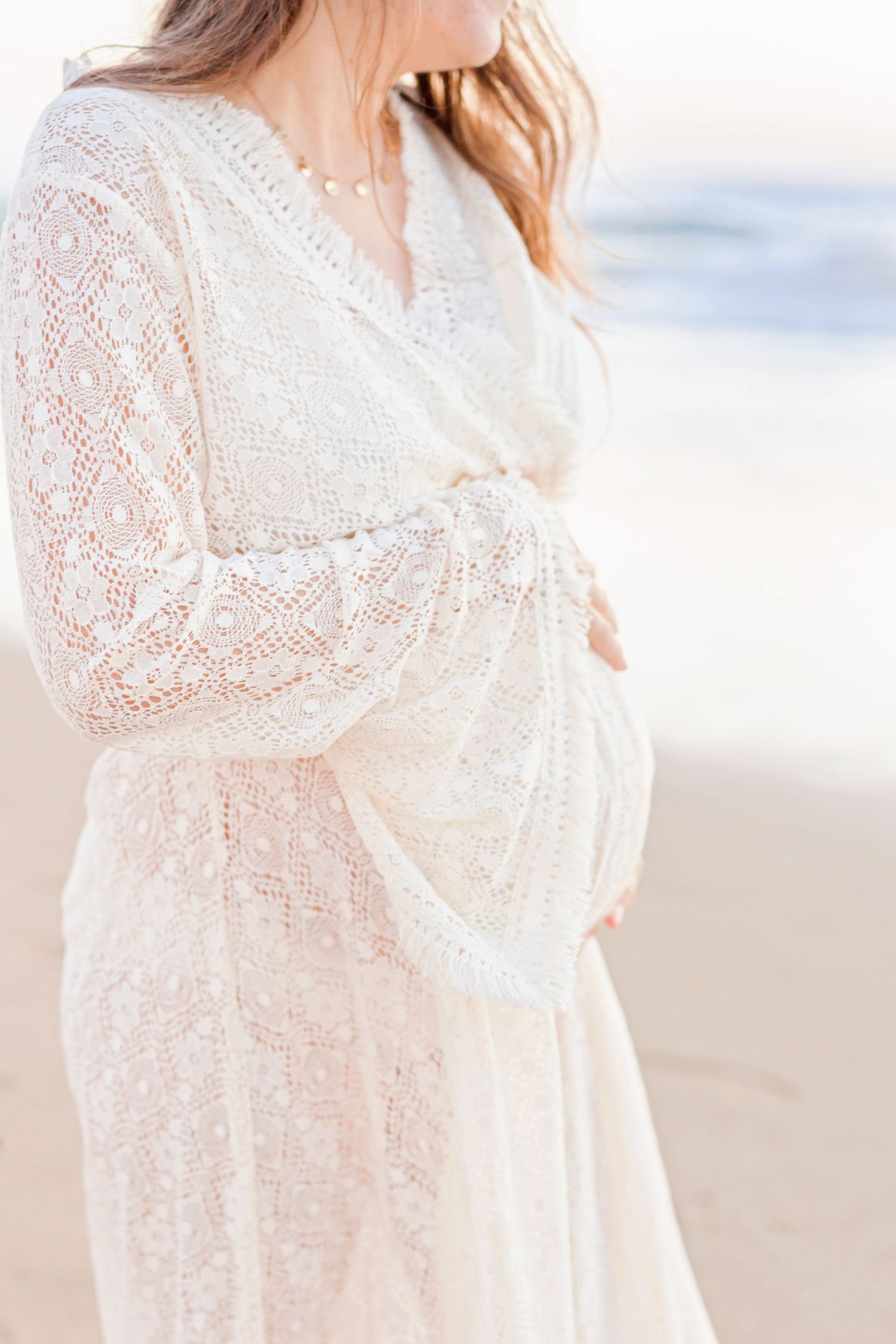 Close-up of a pregnant belly in a delicate white lace maternity dress.