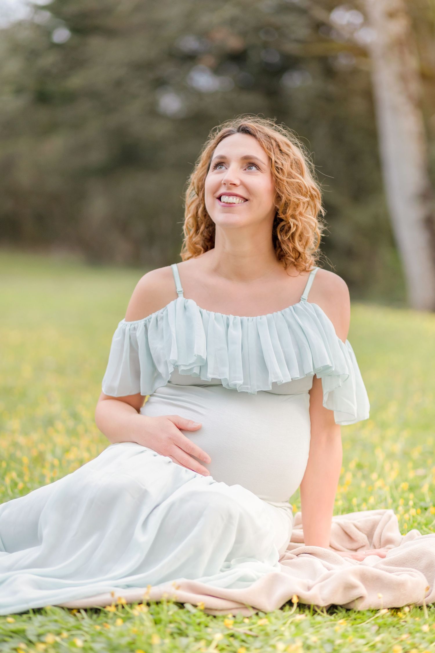 A joyful maternity portrait taken in a sunny meadow with a ruffled white dress.