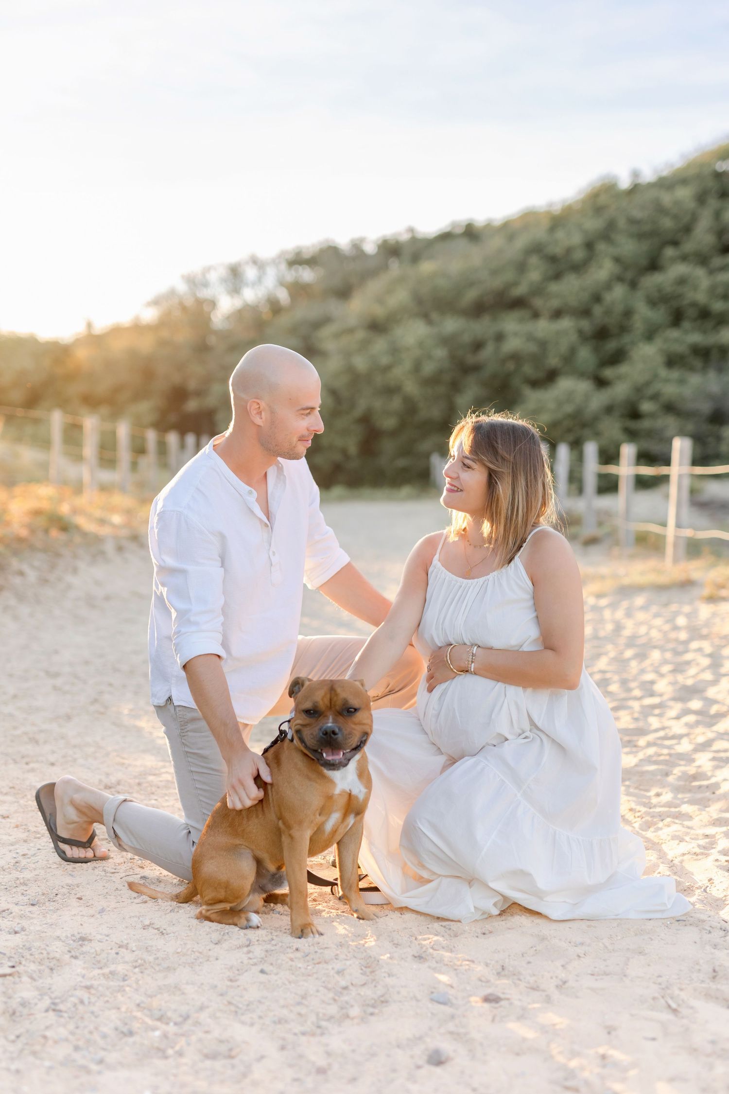Family sits with their brown dog on beach during sunset photoshoot.