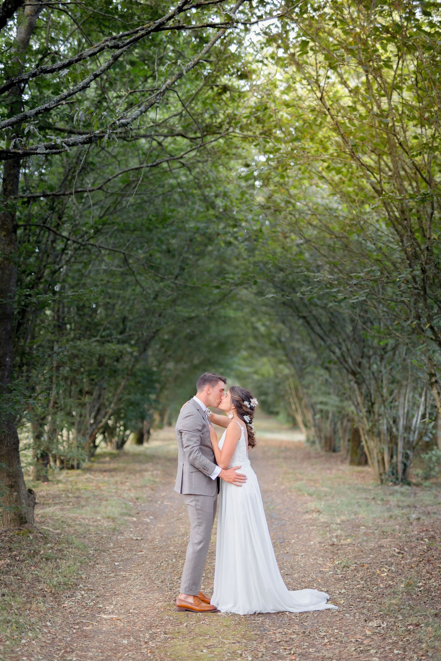 Wedding couple sharing intimate moment in tree-lined pathway with natural lighting.
