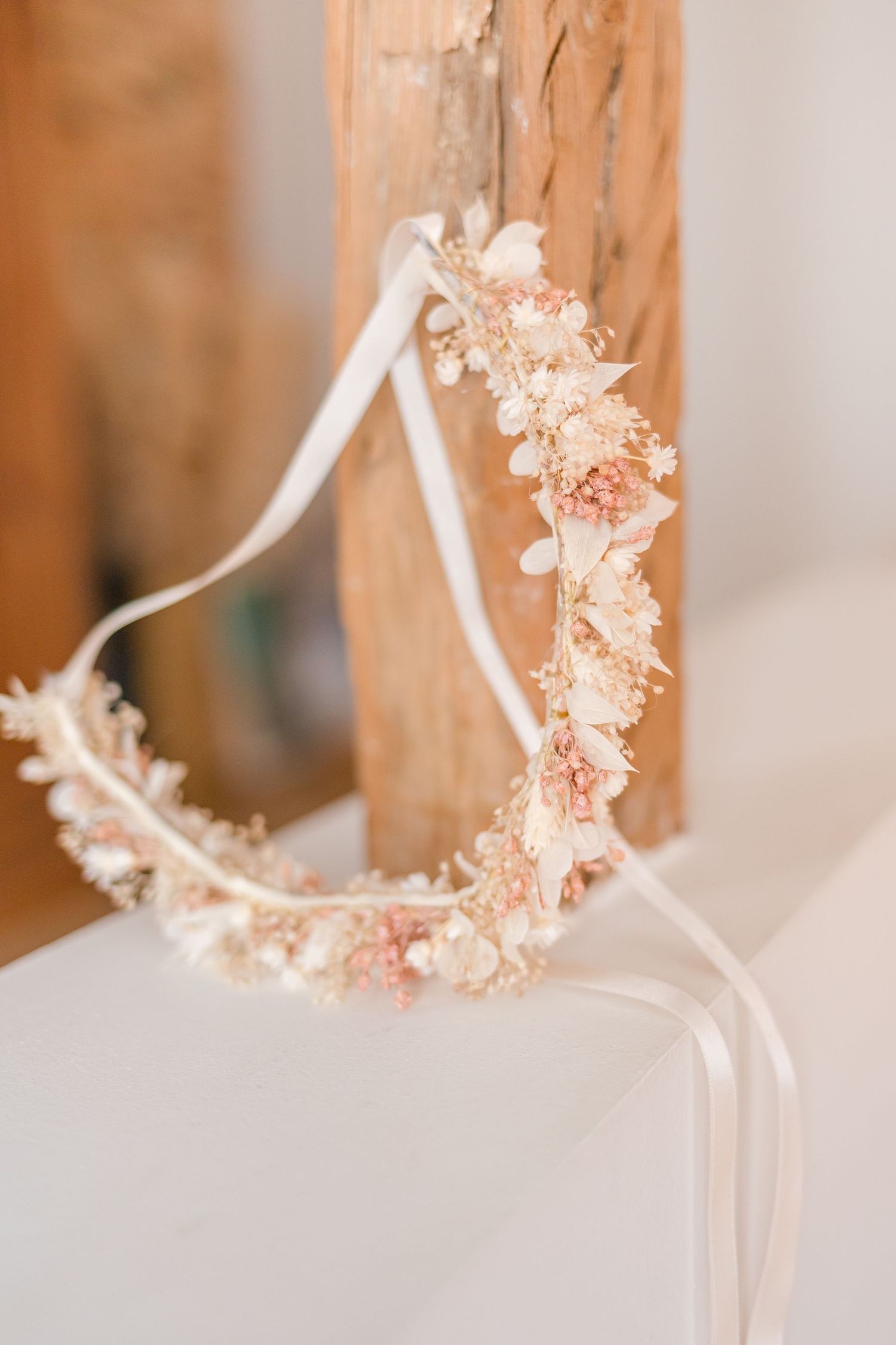 Delicate dried flower crown in soft peach tones hanging against white wall.