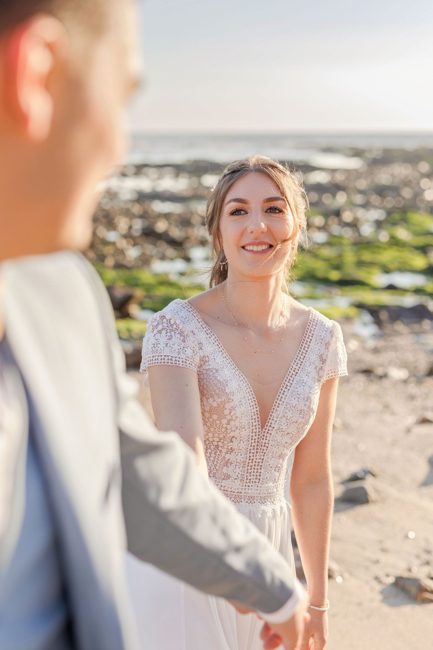 A couple shares a joyful moment on a rocky beach during their wedding photoshoot.