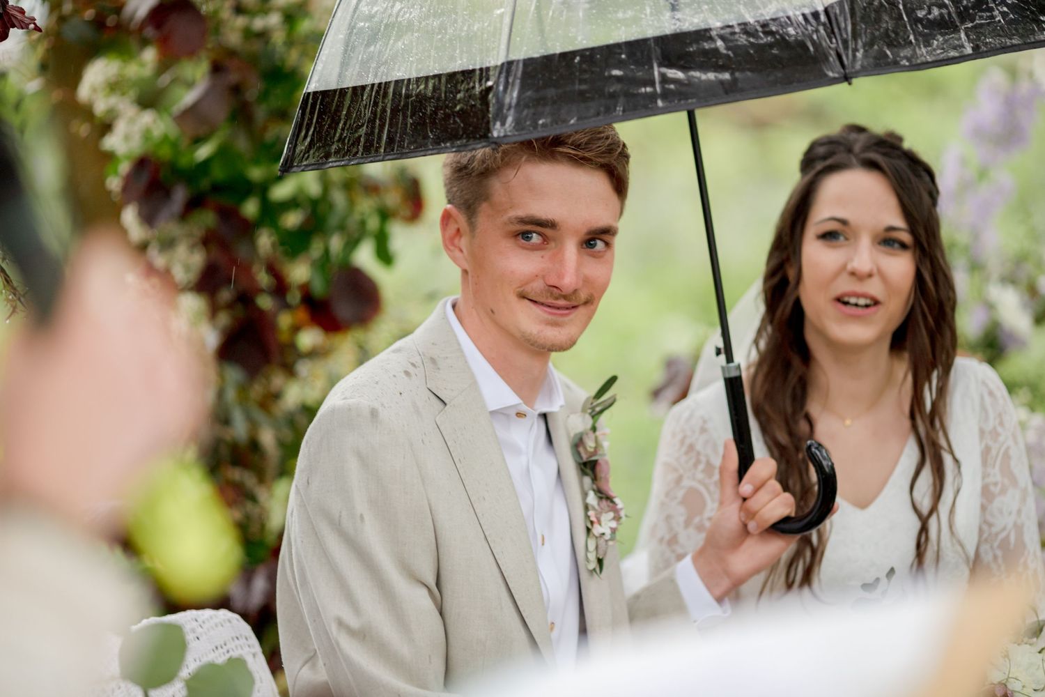 Couple shares romantic moment under umbrella in forest setting.