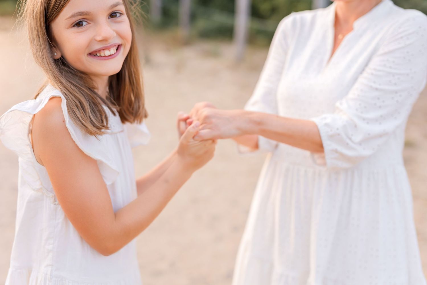 Two people in white dresses holding hands together in a sunny outdoor setting.