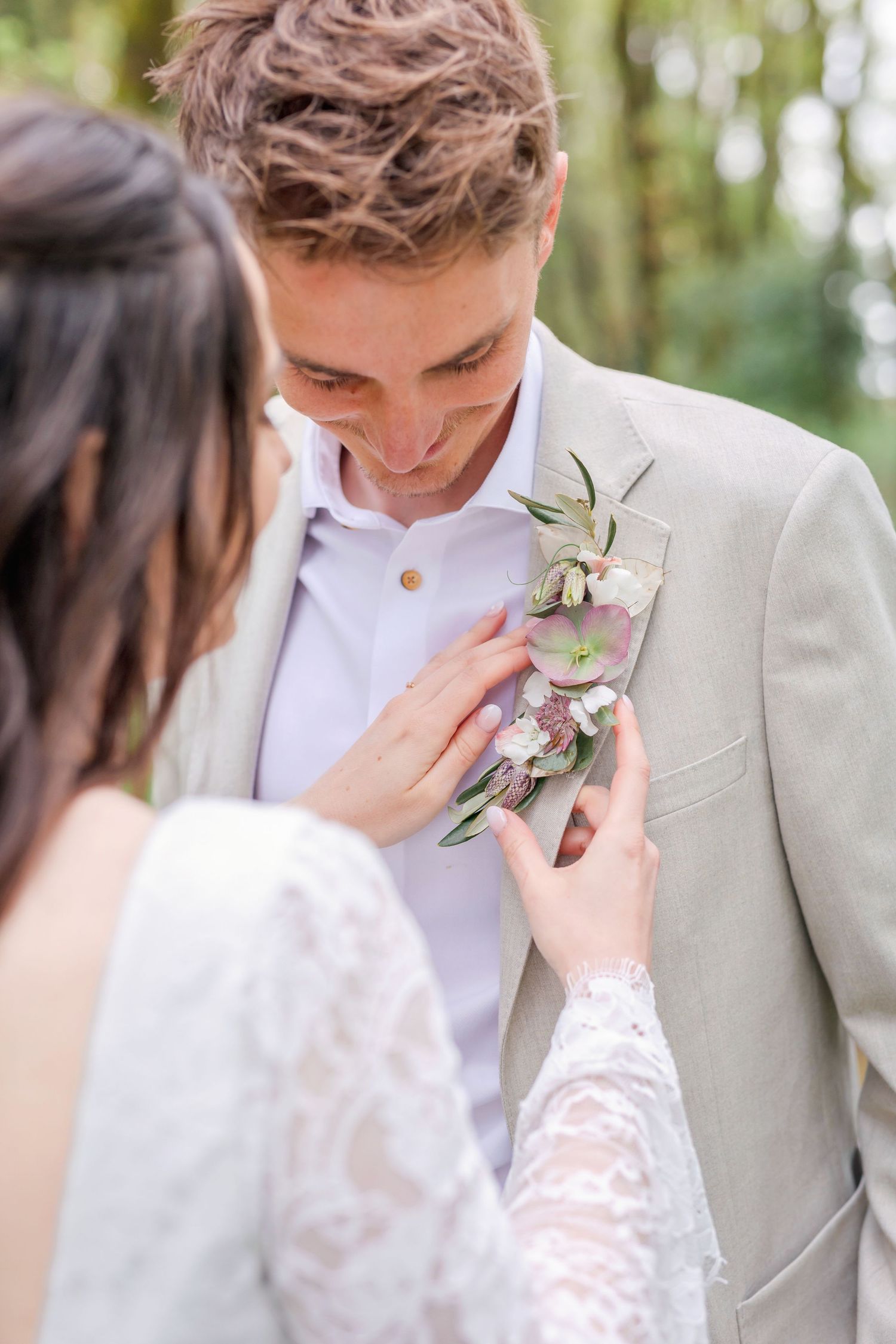 Close up of wedding couple as bride adjusts groom's floral boutonniere on his light beige suit.