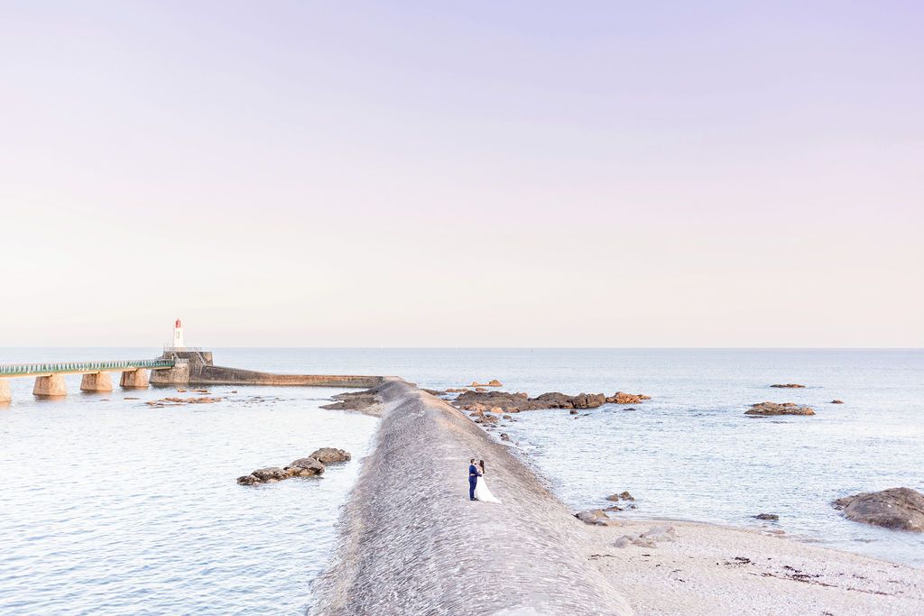 Scenic coastal landscape with lighthouse and rocky breakwater extending into blue ocean.