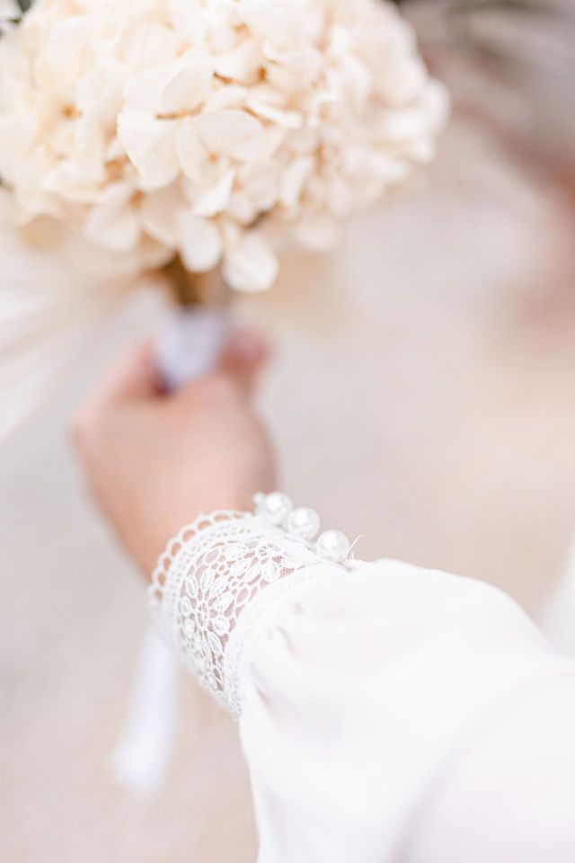 White lace sleeve detail with dried floral bouquet in background.